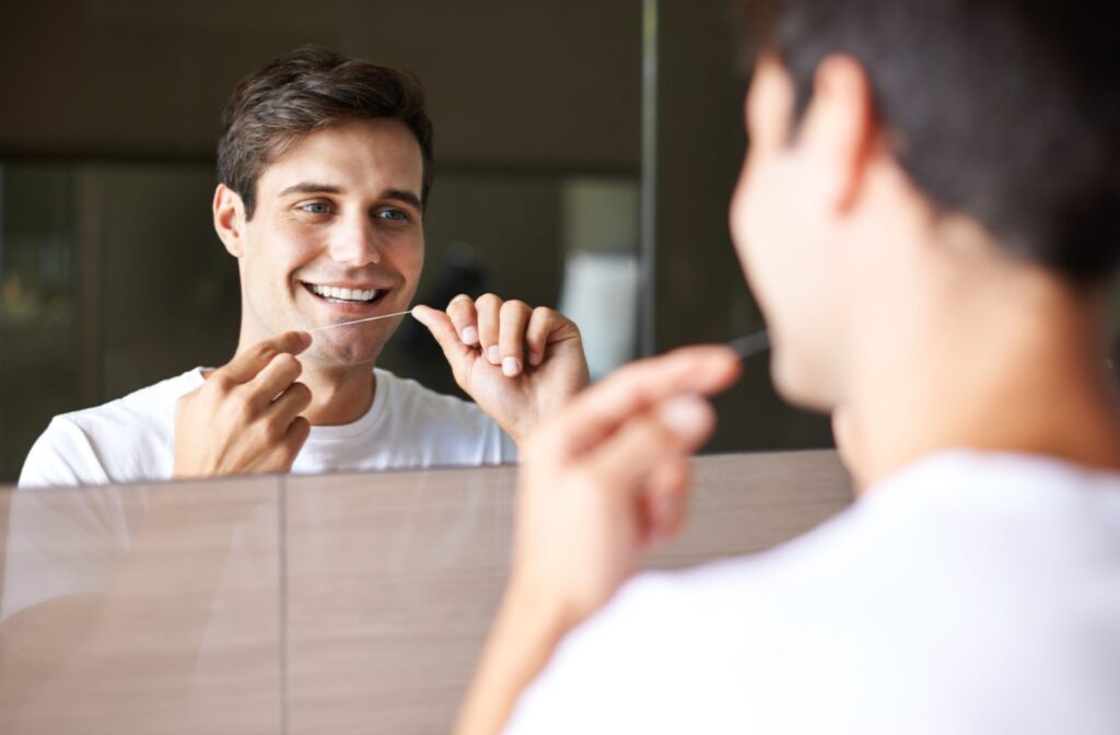 A person looking in the mirror, flossing their teeth to help combat the build up of dental plaque.